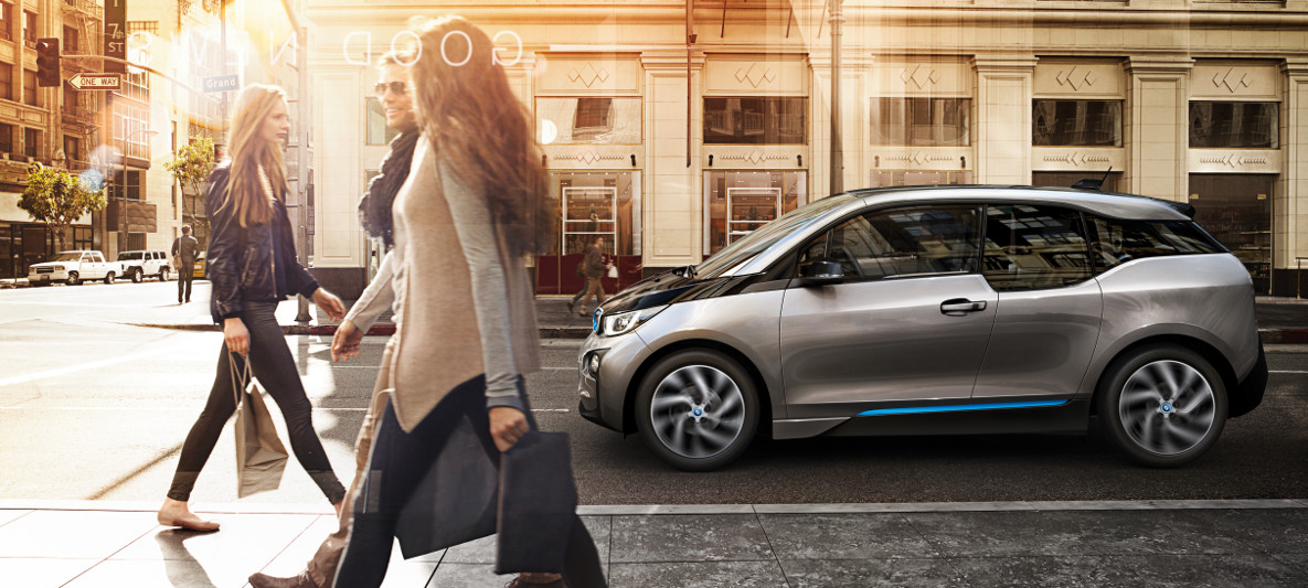 BMW i3 trafegando pela cidade com três pessoas caminhando pela calçada BMW i3 trafegando pela cidade com três pessoas caminhando pela calçada